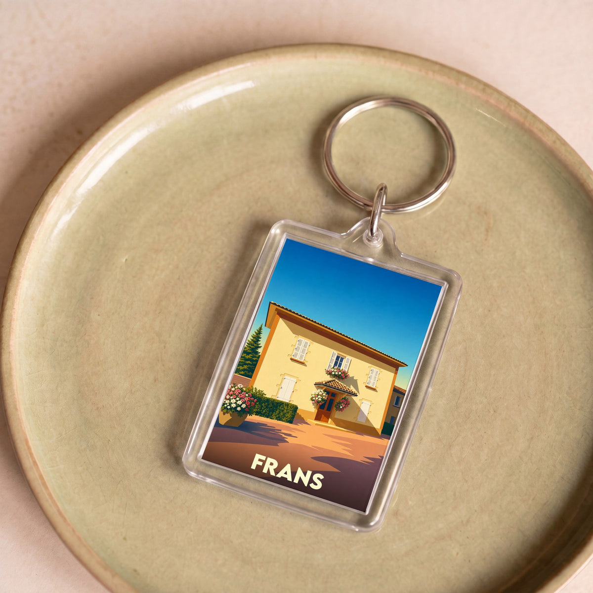 Porte-clés souvenir de la ville de Frans avec une illustration stylisée d'une maison ensoleillée.