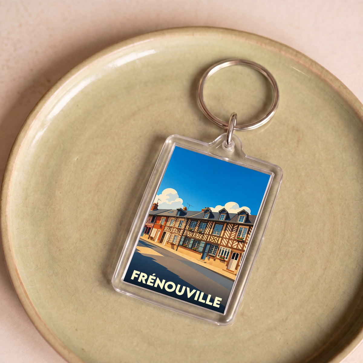 Porte-clés souvenir de la ville de Frénouville avec une illustration stylisée de maisons à colombages.
