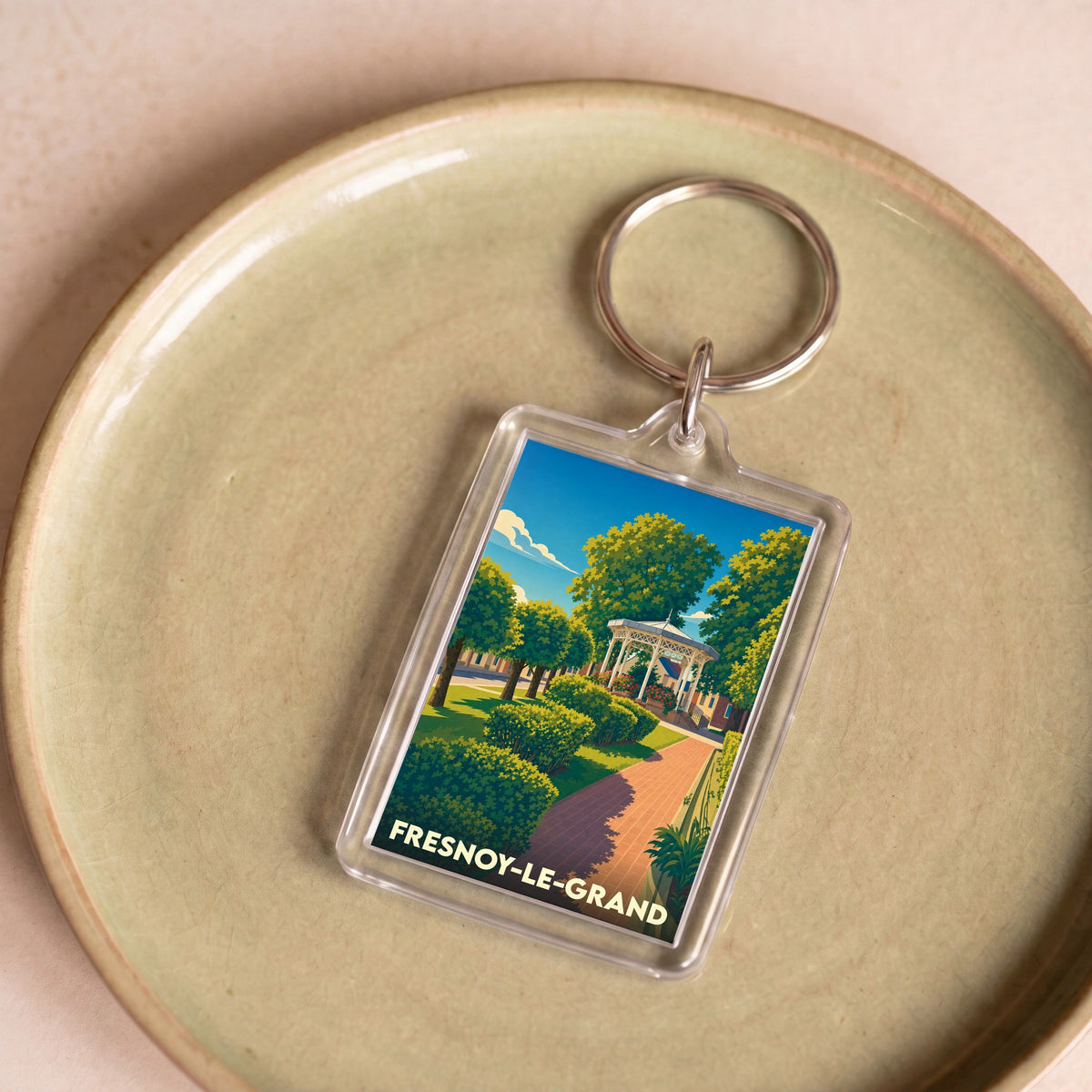 Porte-clés souvenir de la ville de Fresnoy-le-Grand avec une illustration stylisée d'un parc et son kiosque.