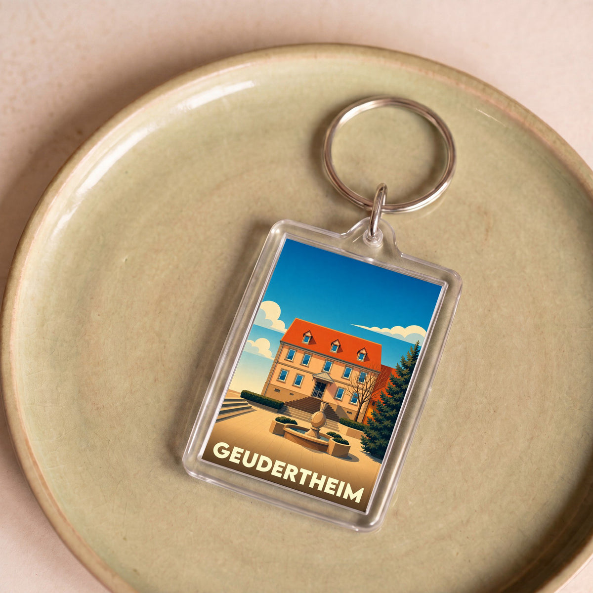 Porte-clés souvenir de la ville de Geudertheim avec une illustration stylisée d'un bâtiment historique et sa fontaine.