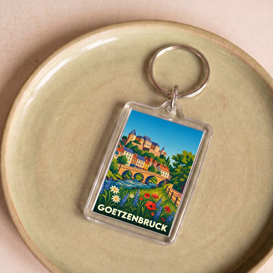 Porte-clés souvenir de la ville de Goetzenbruck avec une illustration colorée et stylisée de son paysage.