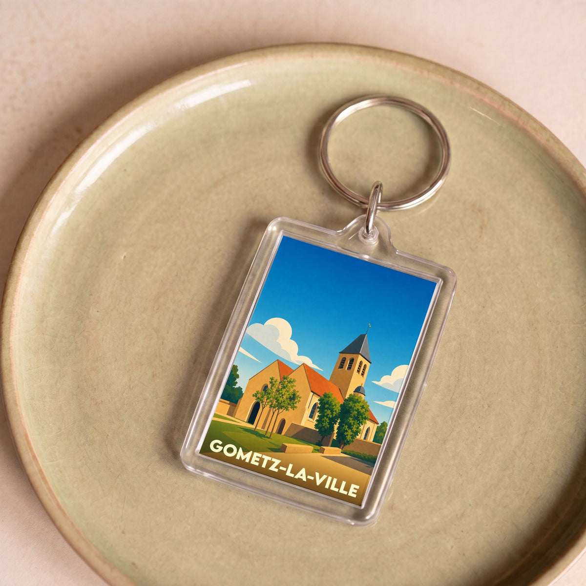Porte-clés souvenir de Gometz-la-Ville avec une illustration stylisée de son église sous un ciel bleu.