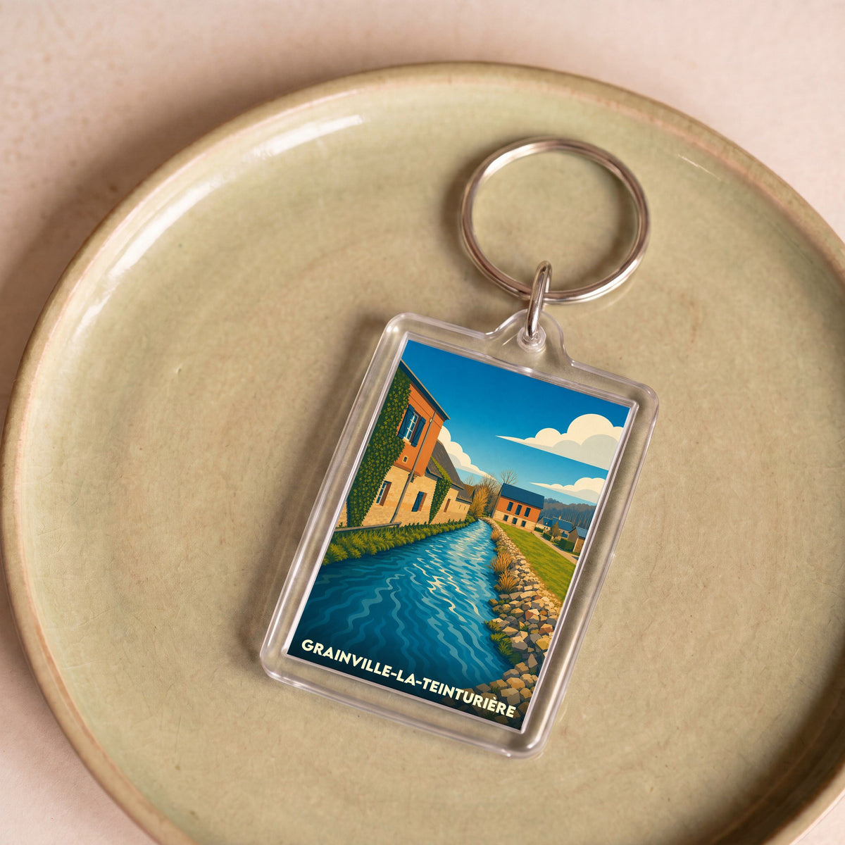Porte-clés souvenir de Grainville-la-Teinturière avec une illustration stylisée de la rivière traversant le village.