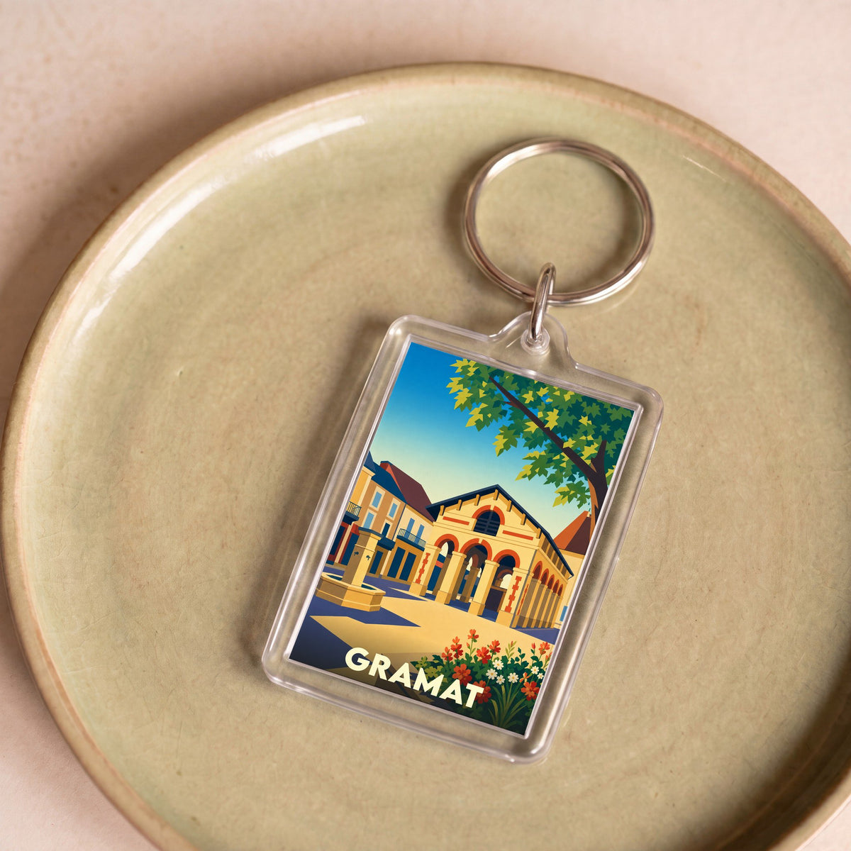Porte-clés souvenir de la ville de Gramat avec une illustration colorée et stylisée de son architecture.