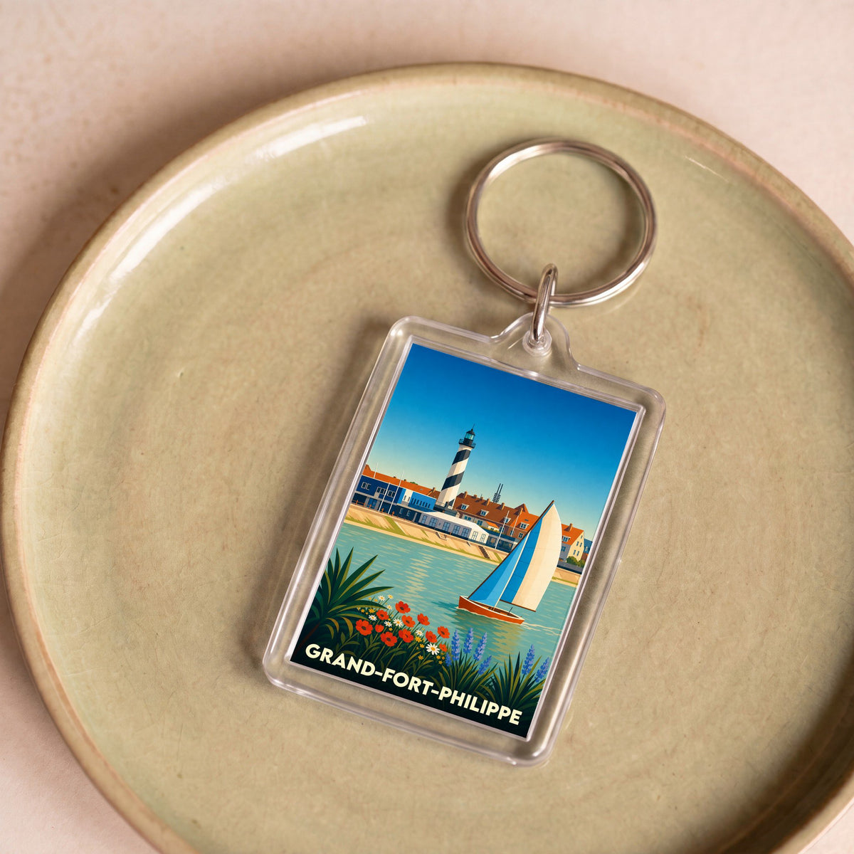 Porte-clés souvenir de Grand-Fort-Philippe avec une illustration stylisée de son phare et d'un voilier.