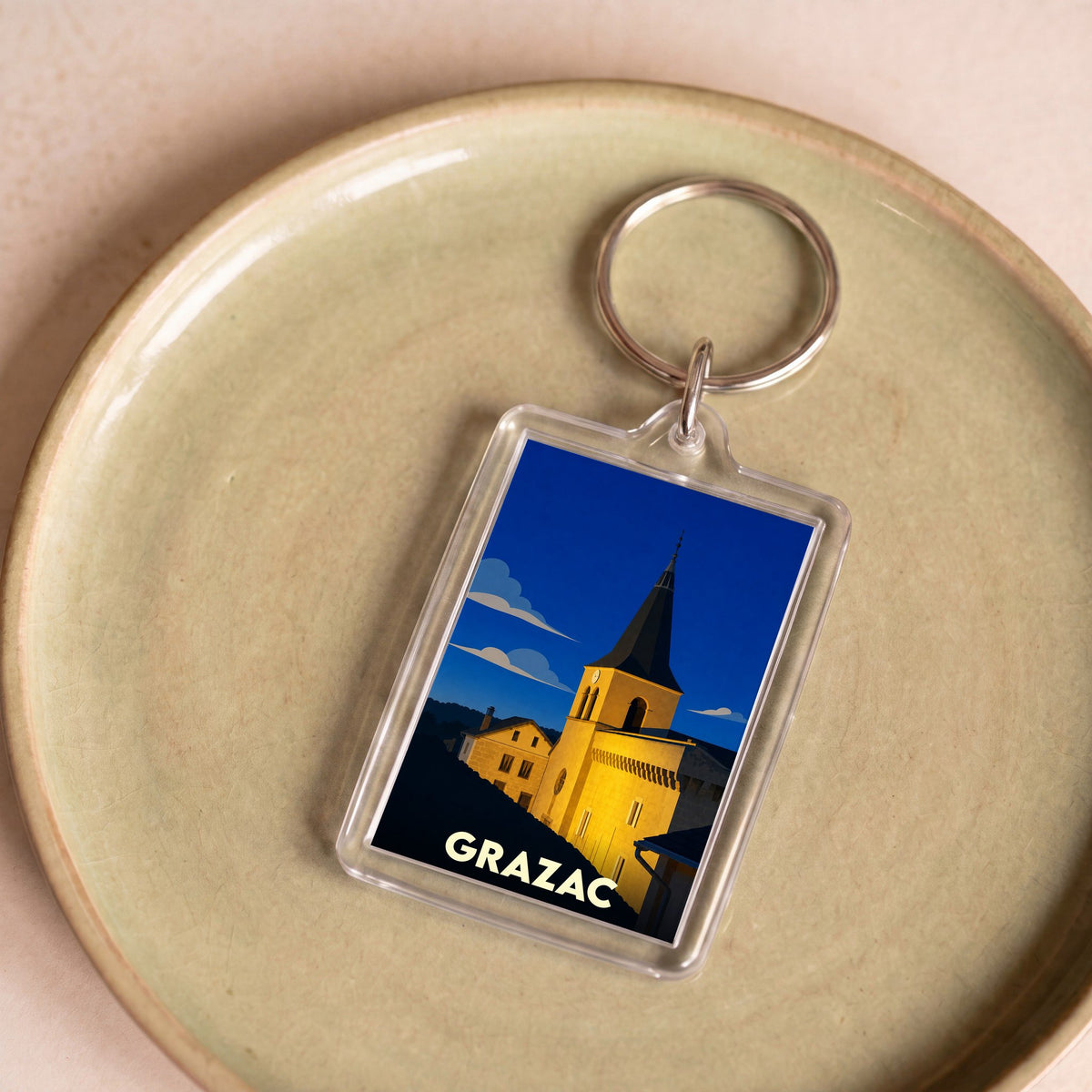 Porte-clés souvenir de la ville de Grazac avec une illustration stylisée de son église sous un ciel nocturne.