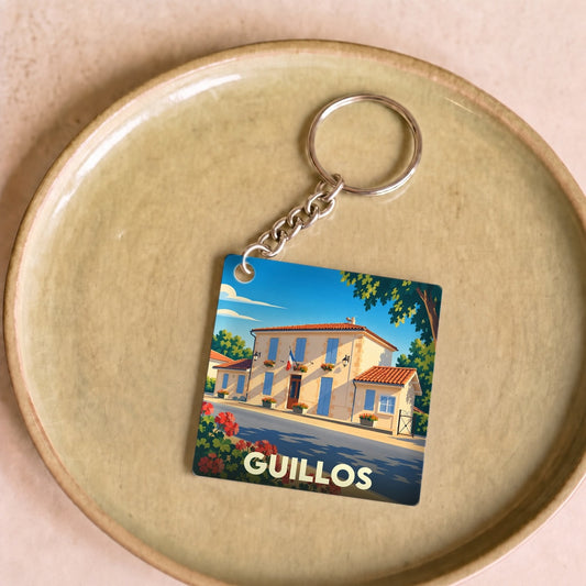 Porte-clés souvenir de la ville de Guillos avec une illustration stylisée d'une bâtisse typique.