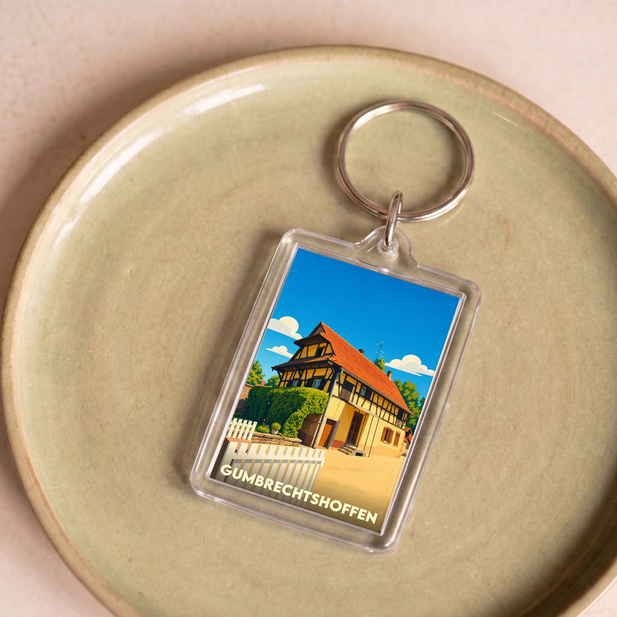Porte-clés souvenir de la ville de Gumbrechtshoffen avec une illustration stylisée d'une maison traditionnelle à colombages.