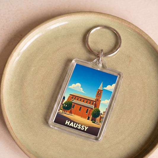 Porte-clés souvenir de la ville de Haussy avec une illustration stylisée d'une église en briques.