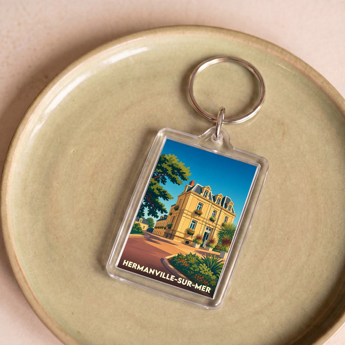 Porte-clés souvenir de la ville de Hermanville-sur-Mer avec une illustration stylisée d'une villa balnéaire.