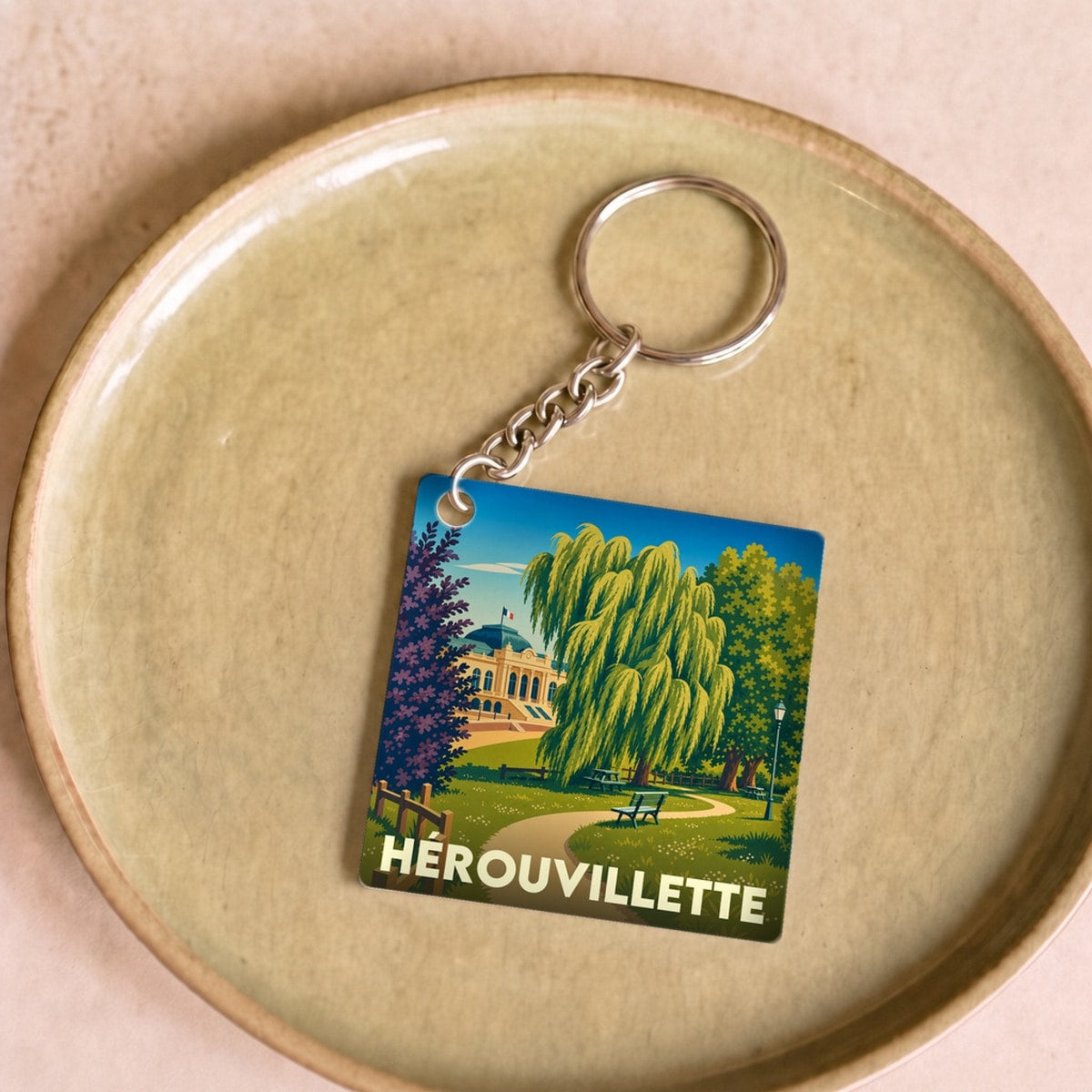 Porte-clés souvenir de la ville de Hérouvillette avec une illustration stylisée d'un parc.