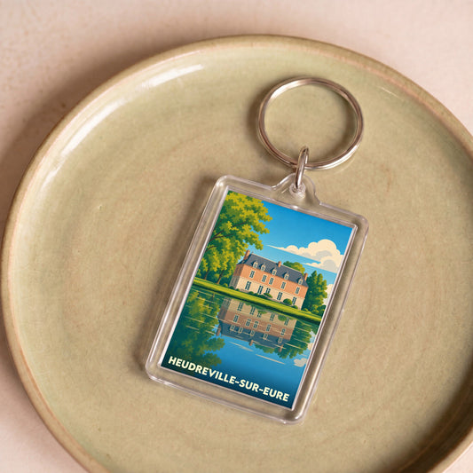 Porte-clés souvenir de la ville de Heudreville-sur-Eure avec une illustration stylisée d'un château se reflétant dans l'eau.
