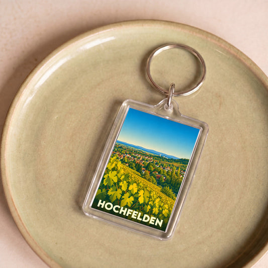 Porte-clés souvenir de la ville de Hochfelden avec une illustration stylisée de vignobles et du village.