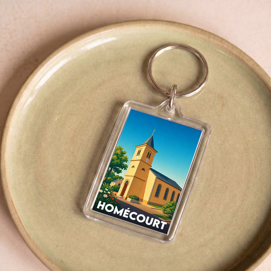 Porte-clés souvenir de la ville de Homécourt avec une illustration stylisée de son église sous un ciel bleu.