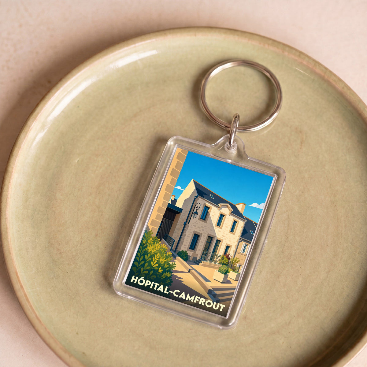 Porte-clés souvenir de la ville de Hôpital-Camfrout avec une illustration stylisée d'une rue ensoleillée.