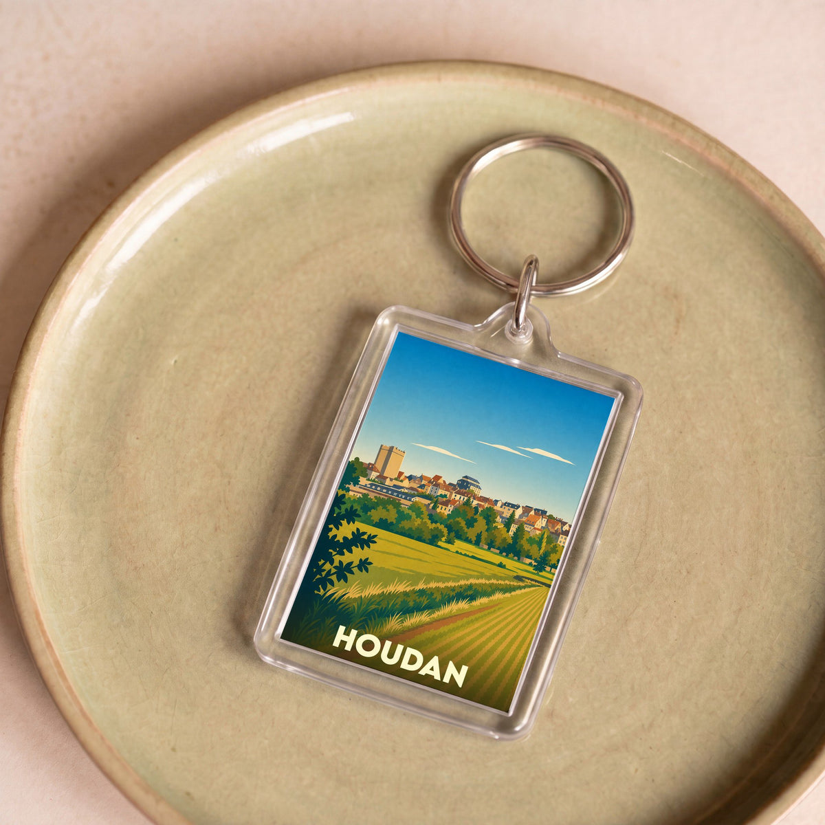 Porte-clés souvenir de la ville de Houdan avec une illustration stylisée de son paysage et de son donjon.