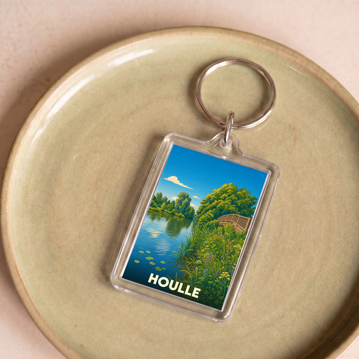 Porte-clés souvenir de la ville de Houlle avec une illustration stylisée représentant un paysage de rivière.