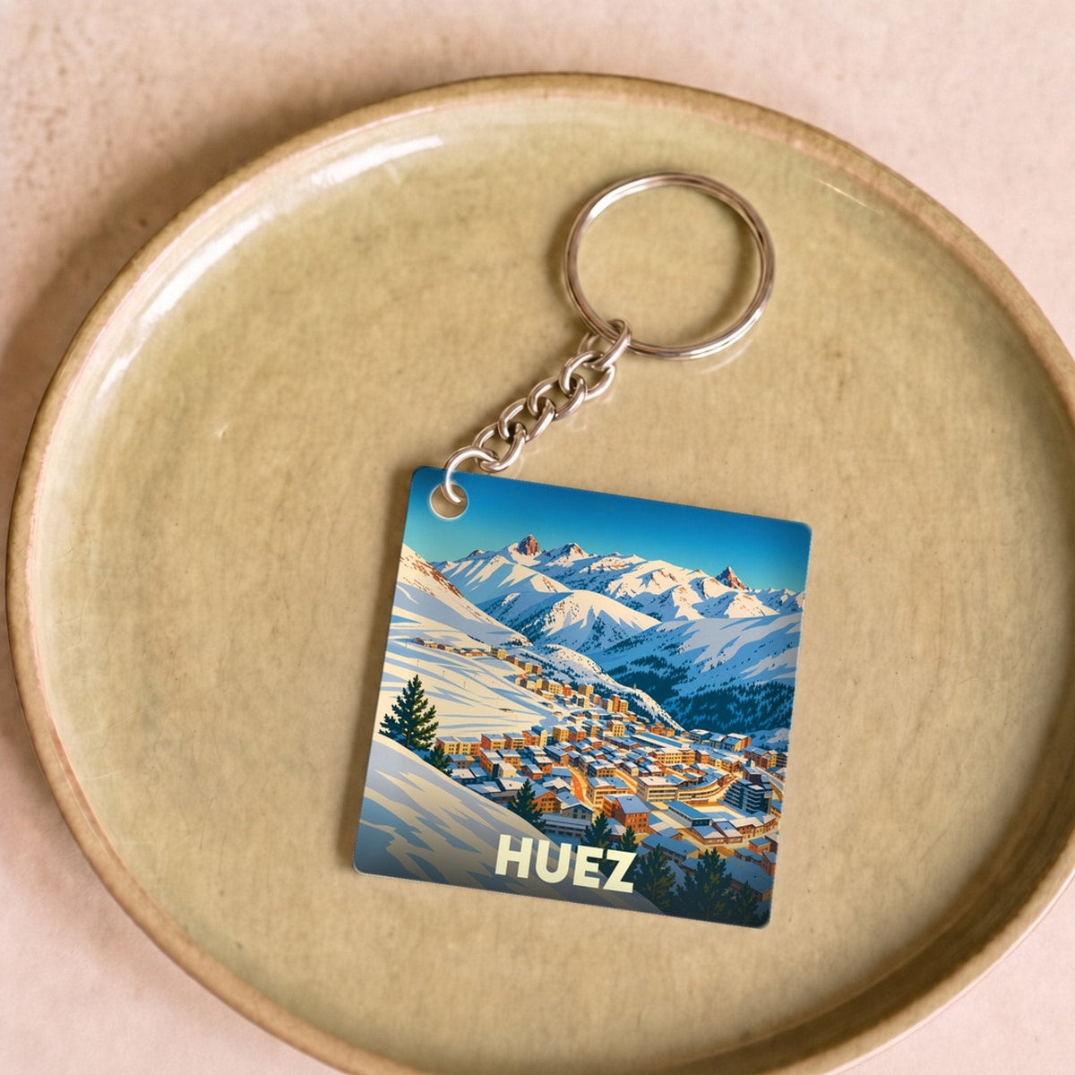 Porte-clés souvenir de la ville de Huez avec une illustration stylisée d'un village de montagne enneigé.