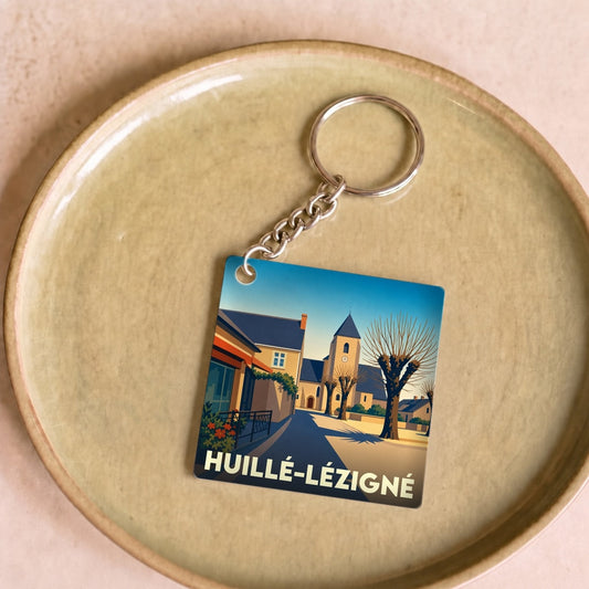 Porte-clés souvenir de la ville de Huillé-Lézigné avec une illustration stylisée de son église et de ses rues.