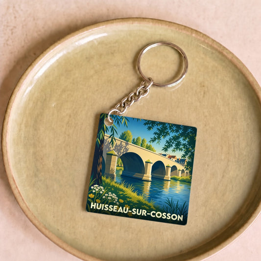 Porte-clés souvenir de la ville de Huisseau-sur-Cosson avec une illustration stylisée d'un pont au bord de l'eau.