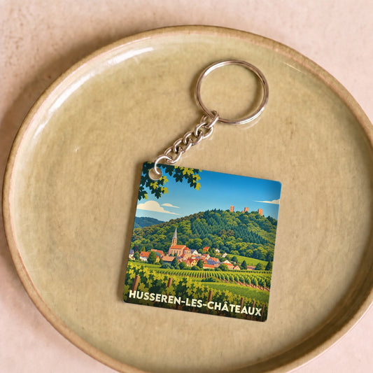 Porte-clés souvenir de Husseren-les-Châteaux avec une illustration stylisée du village et de ses vignobles.