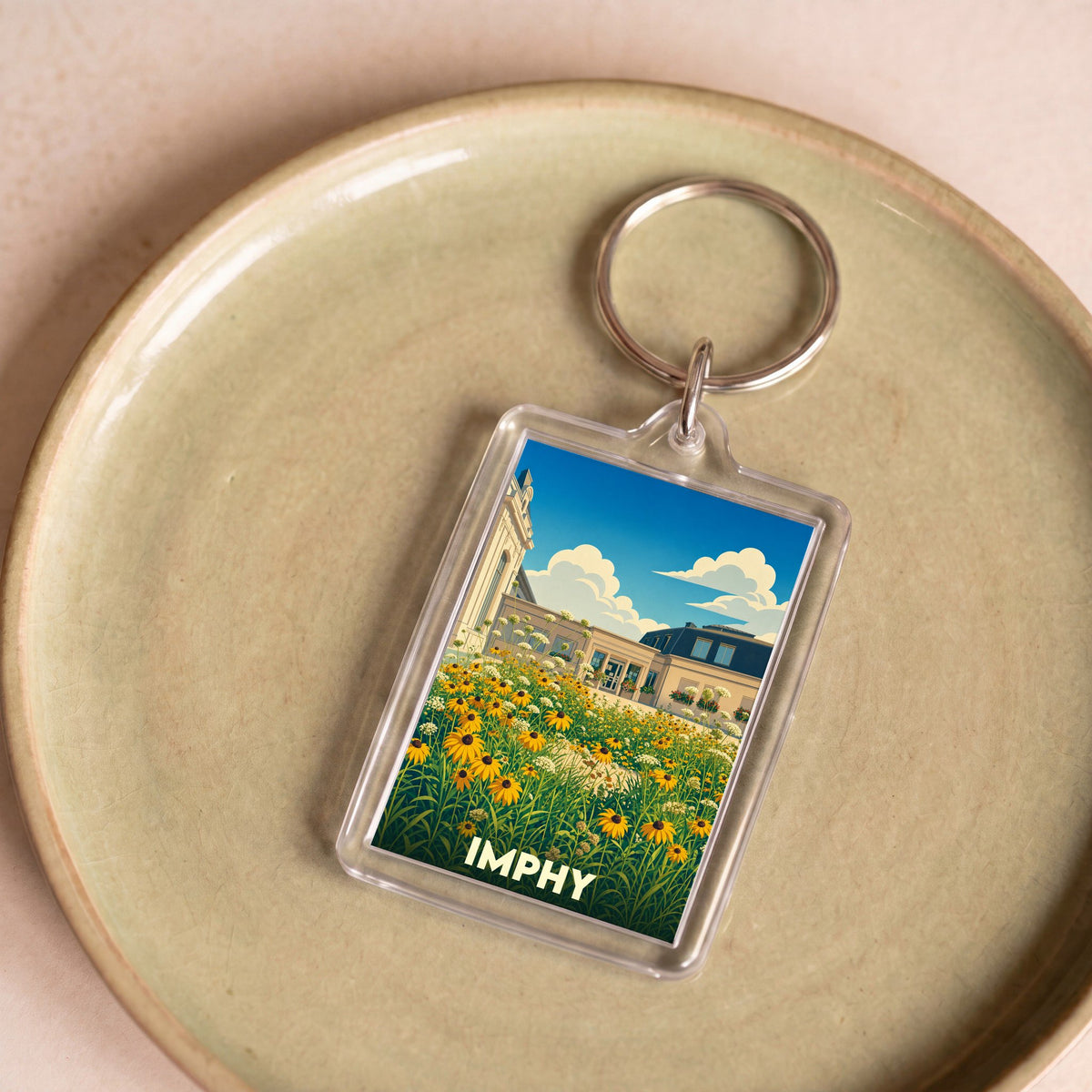 Porte-clés souvenir de la ville d'Imphy avec une illustration stylisée d'un jardin fleuri devant des bâtiments.