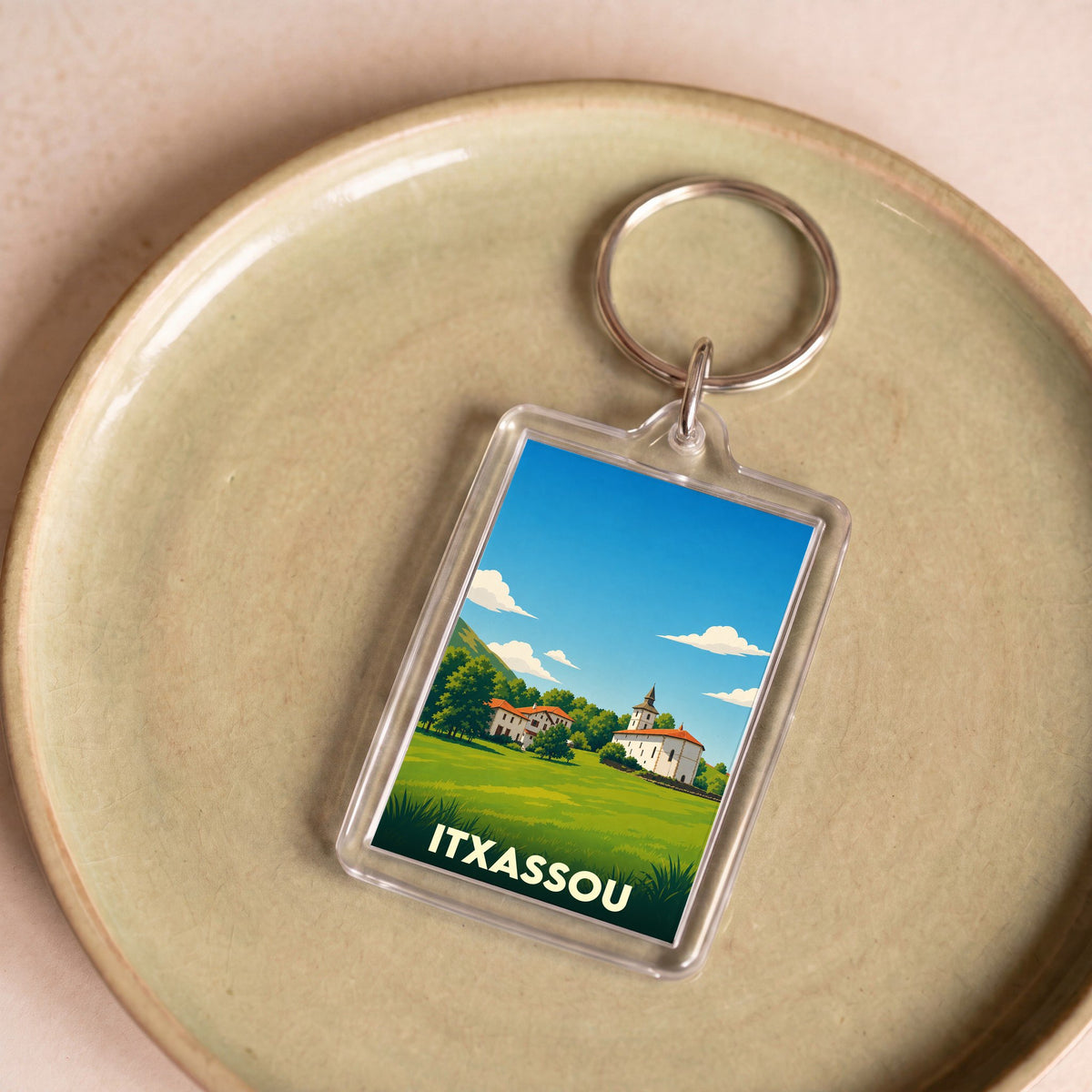 Porte-clés souvenir de la ville d'Itxassou avec une illustration stylisée d'un paysage basque.