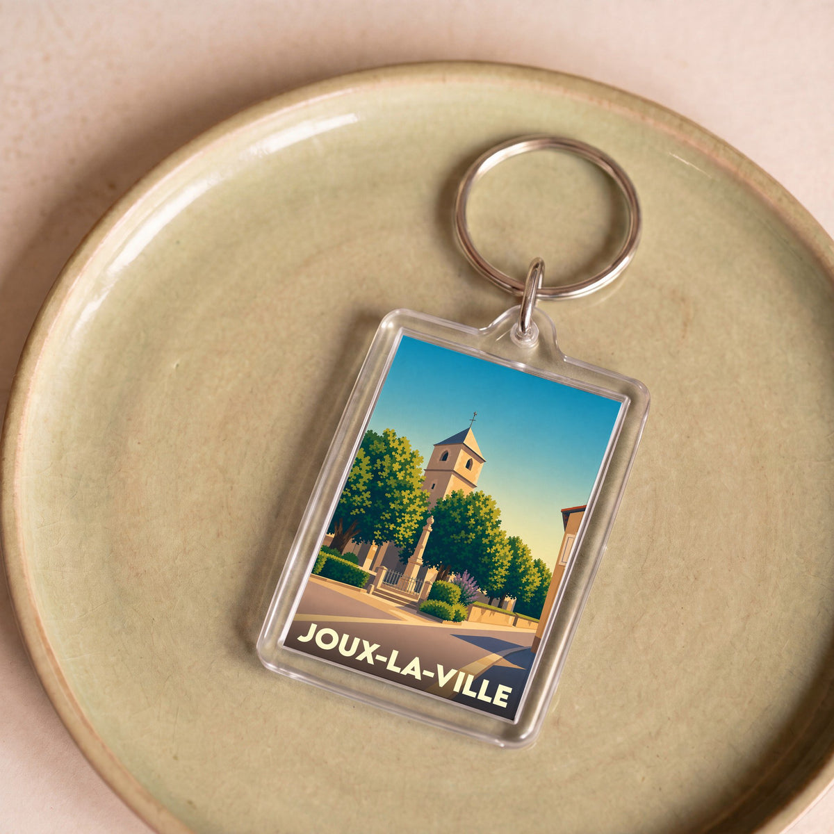 Porte-clés souvenir de Joux-la-Ville avec une illustration stylisée d'une église et d'une place arborée.