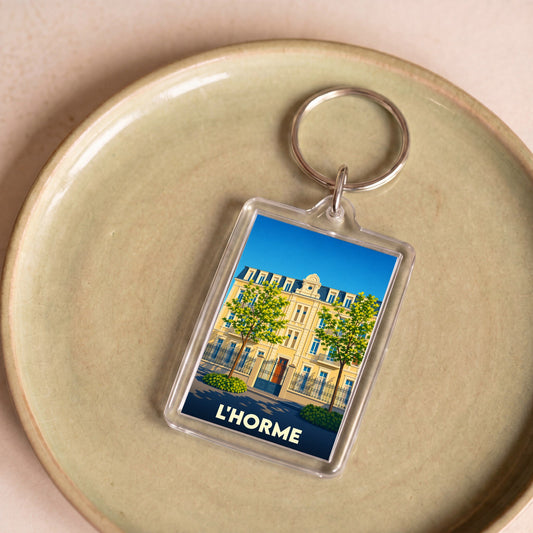 Porte-clés souvenir de la ville de L'Horme avec une illustration stylisée d'un bâtiment classique.