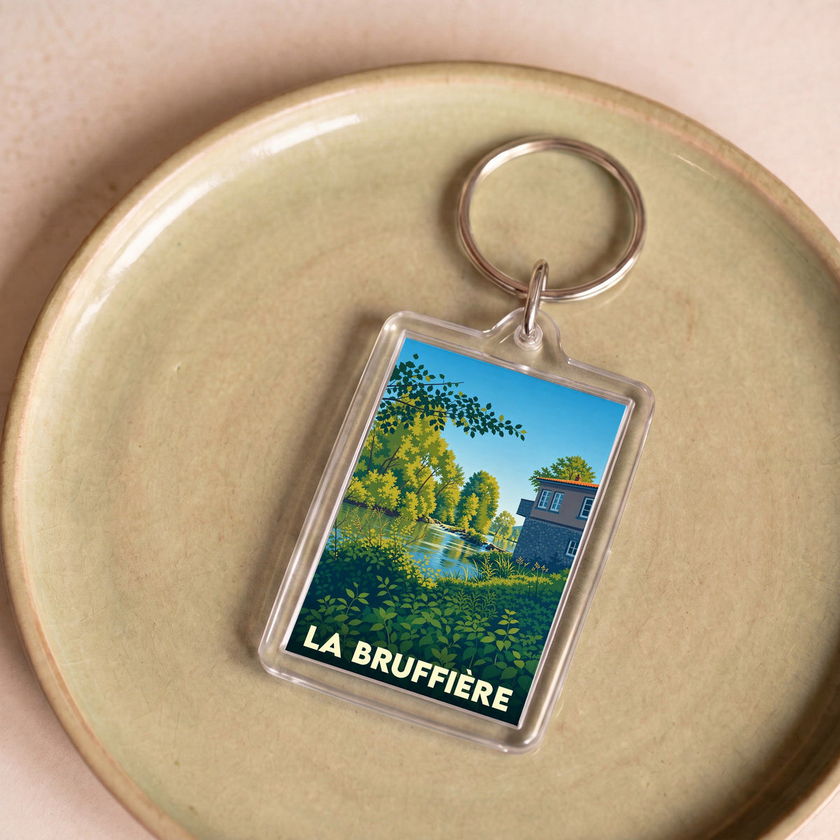 Porte-clés souvenir de la ville de La Bruffière avec une illustration stylisée d'un paysage de bord de rivière.