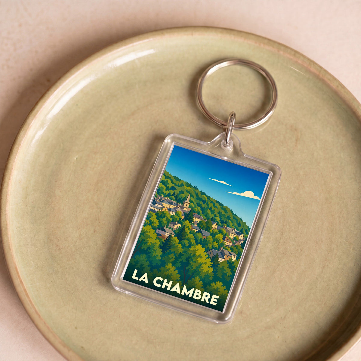 Porte-clés souvenir de la ville de La Chambre avec une illustration stylisée d'un village niché dans une colline verdoyante.