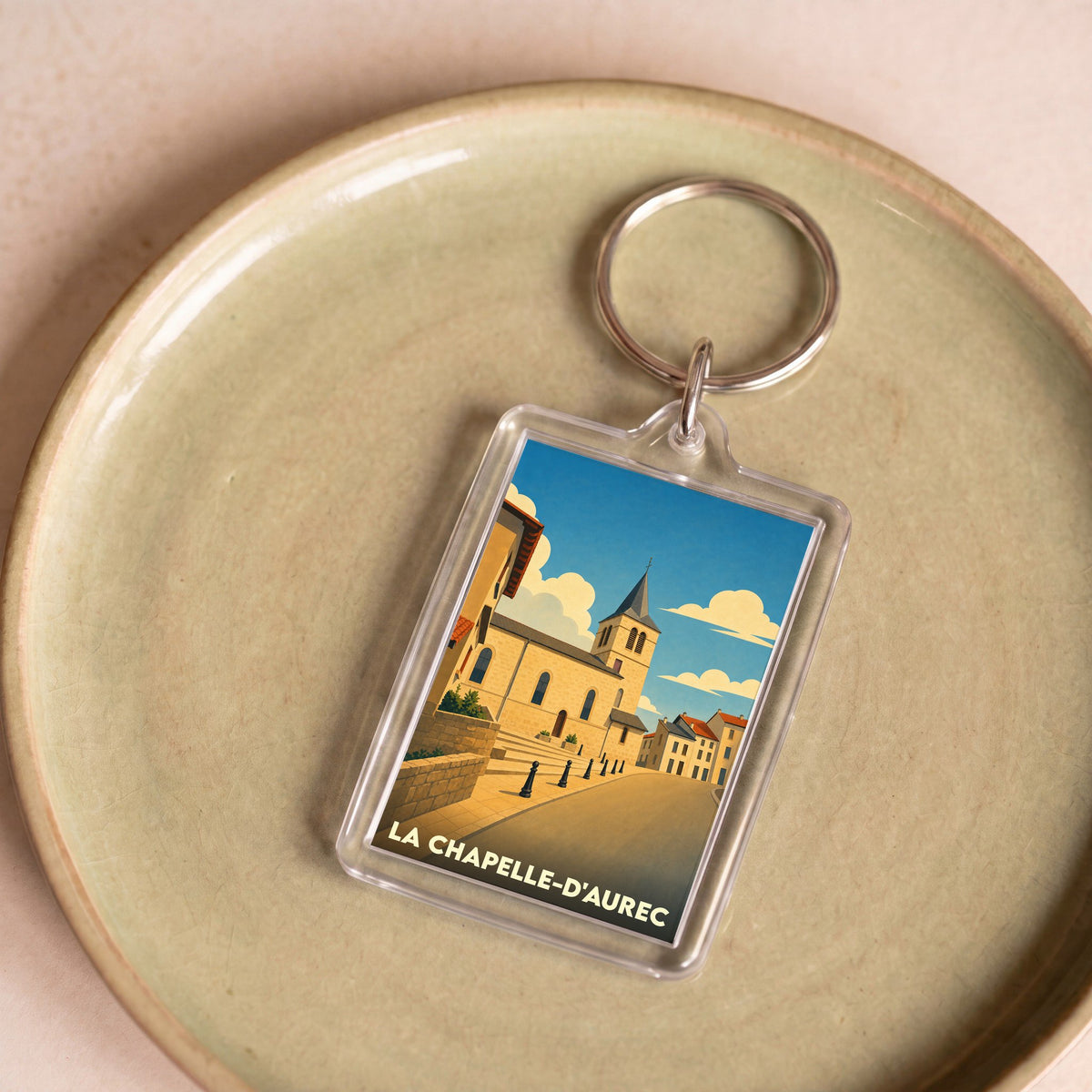 Porte-clés souvenir de la ville de La Chapelle-d'Aurec avec une illustration stylisée d'une église sous un ciel bleu.
