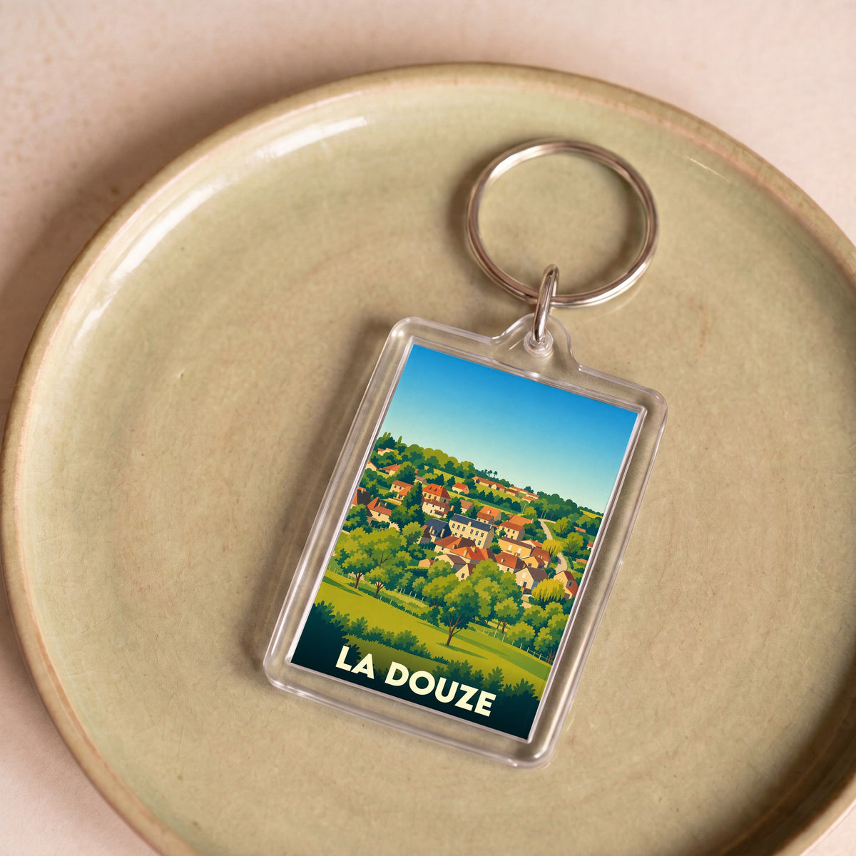 Porte-clés souvenir de la ville de La Douze avec une illustration stylisée d'un village vallonné.