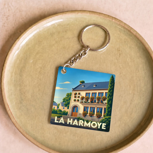 Porte-clés souvenir de la ville de La Harmoye avec une illustration stylisée d'une maison fleurie.
