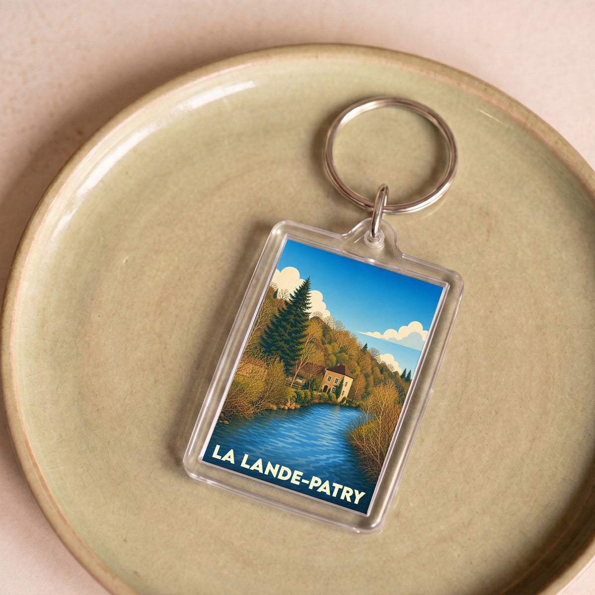 Porte-clés souvenir de la ville de La Lande-Patry avec une illustration stylisée de paysage.