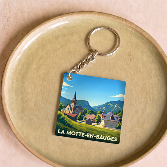 Porte-clés souvenir de la ville de La Motte-en-Bauges avec une illustration stylisée d'un village de montagne.