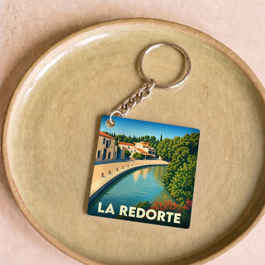 Porte-clés souvenir de la ville de La Redorte avec une illustration stylisée du canal et de ses maisons.