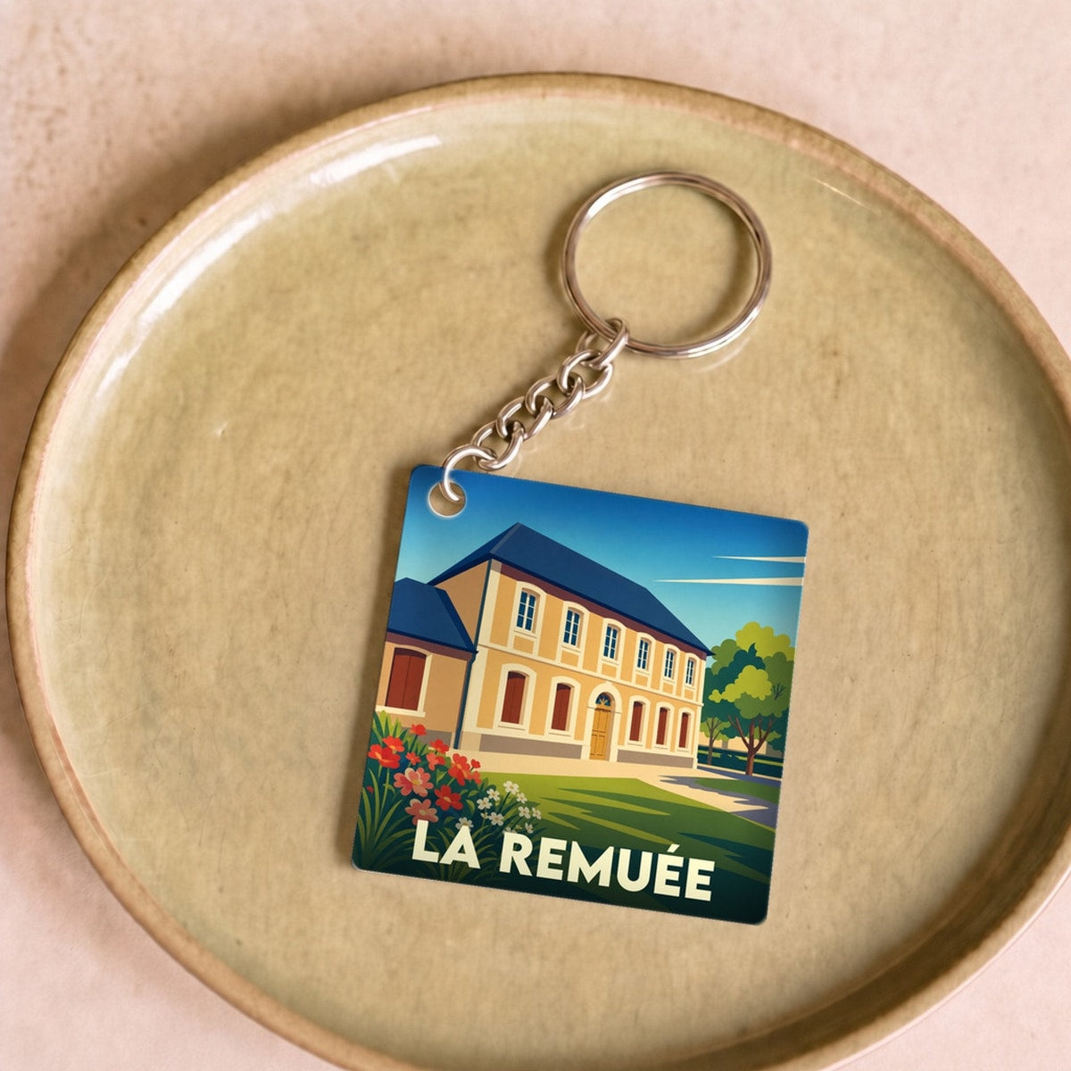 Porte-clés souvenir de la ville de La Remuée avec une illustration stylisée d'une bâtisse traditionnelle.