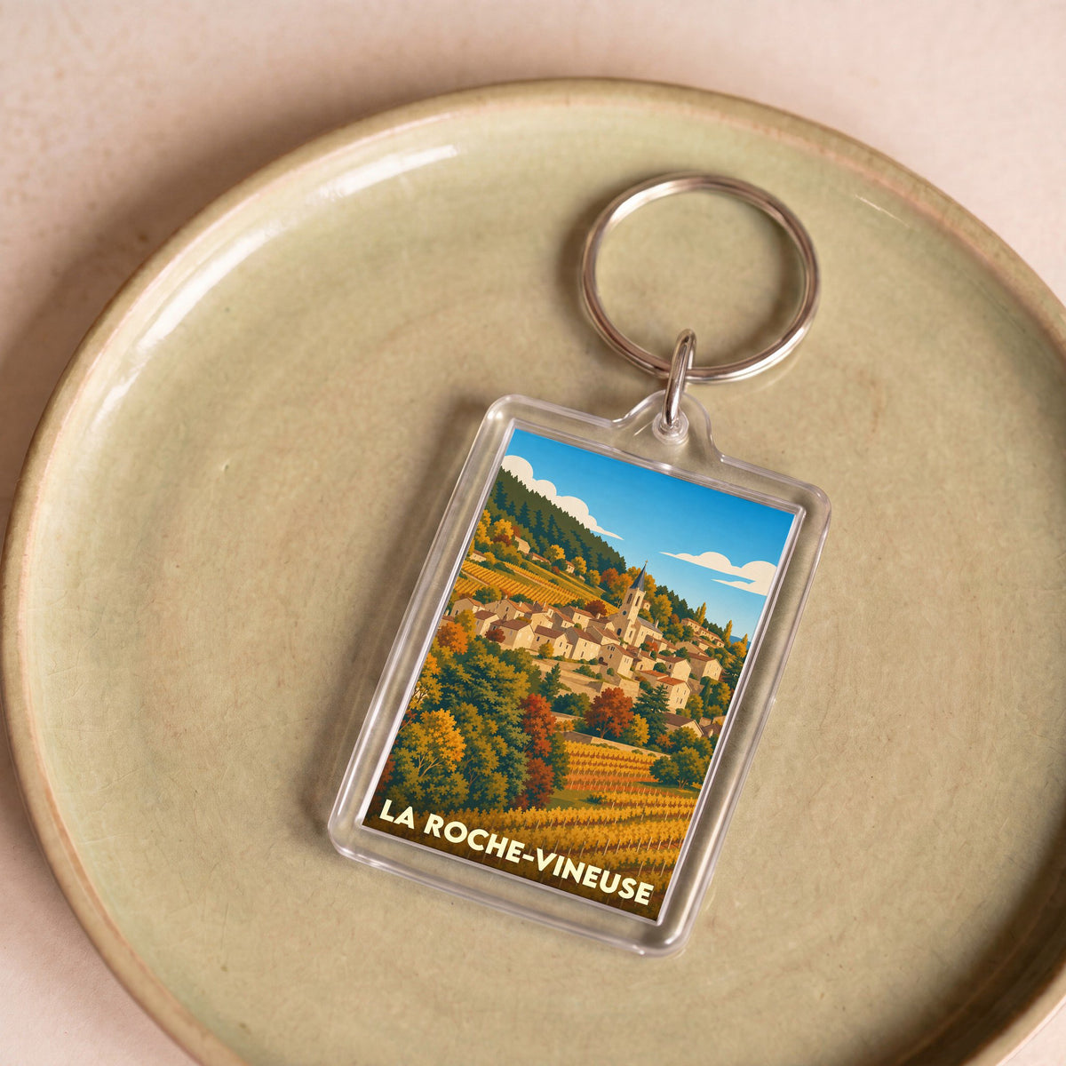 Porte-clés souvenir de la ville de La Roche-Vineuse avec une illustration stylisée de son paysage de vignes et de son village.