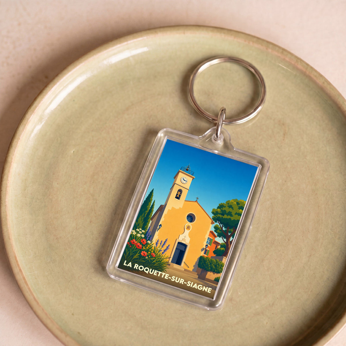 Porte-clés souvenir de la ville de La Roquette-sur-Siagne avec une illustration stylisée de son église provençale.