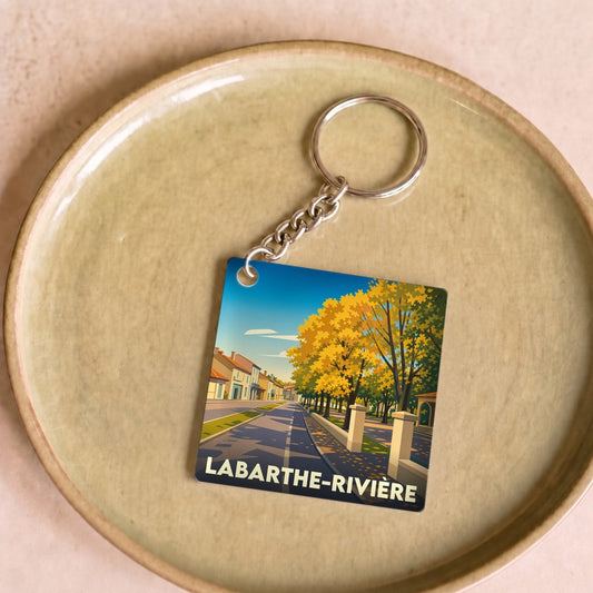 Porte-clés souvenir de la ville de Labarthe-Rivière avec une illustration stylisée d'une rue bordée d'arbres en automne.