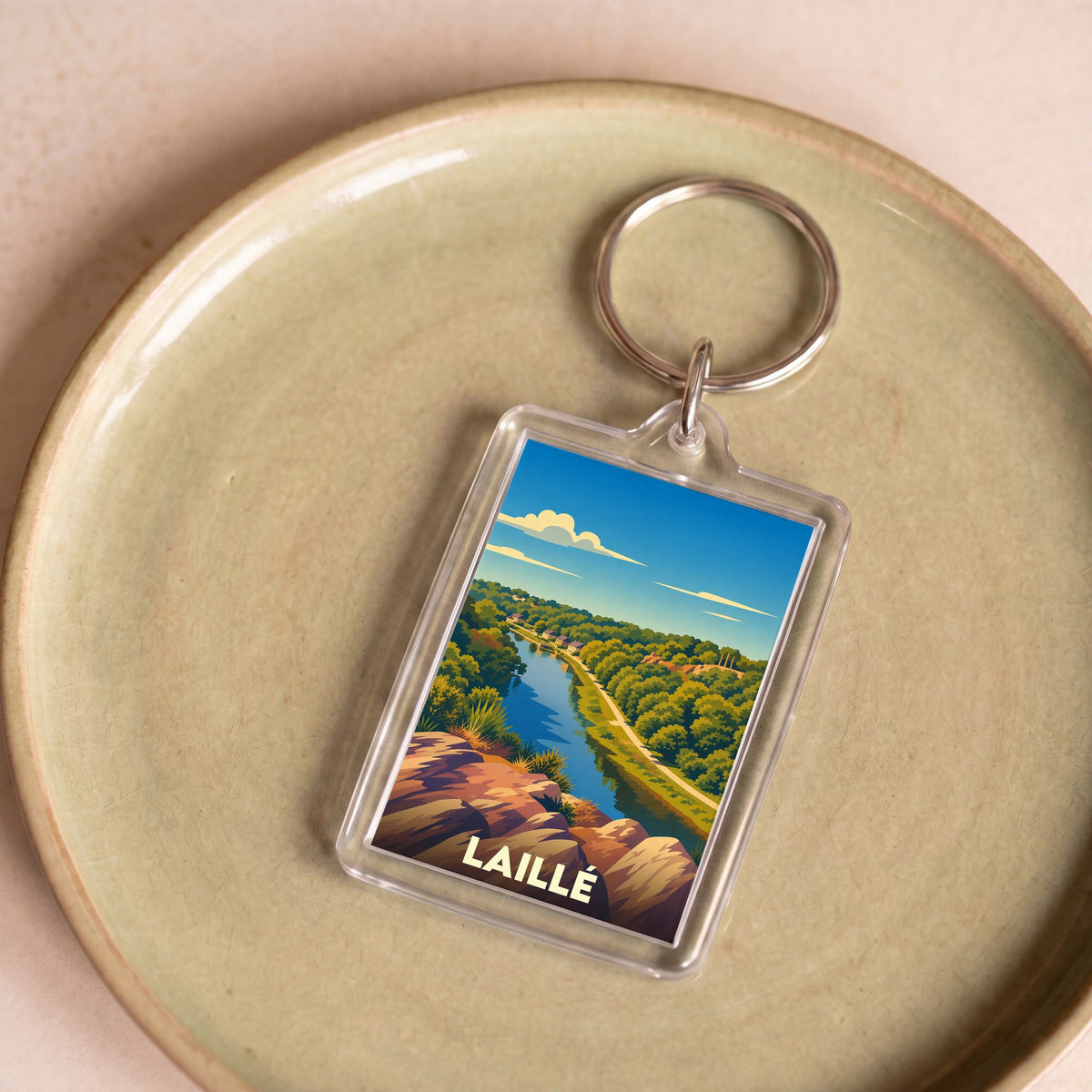Porte-clés souvenir de la ville de Laillé avec une illustration stylisée d'un paysage de rivière.
