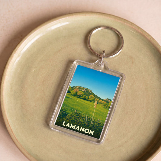 Porte-clés souvenir de la ville de Lamanon avec une illustration stylisée de son paysage champêtre.