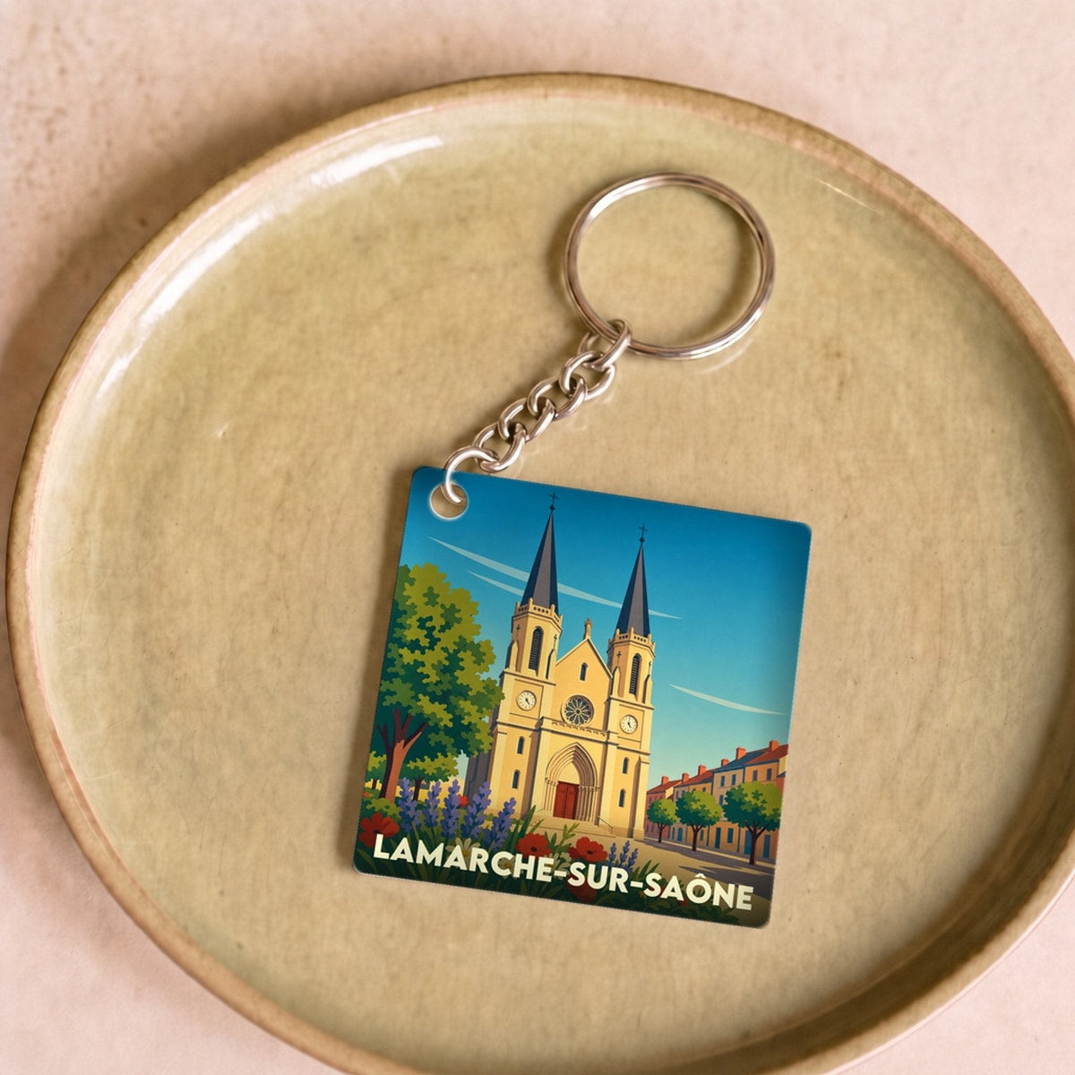 Porte-clés souvenir de la ville de Lamarche-sur-Saône avec une illustration stylisée de son église et de fleurs colorées.