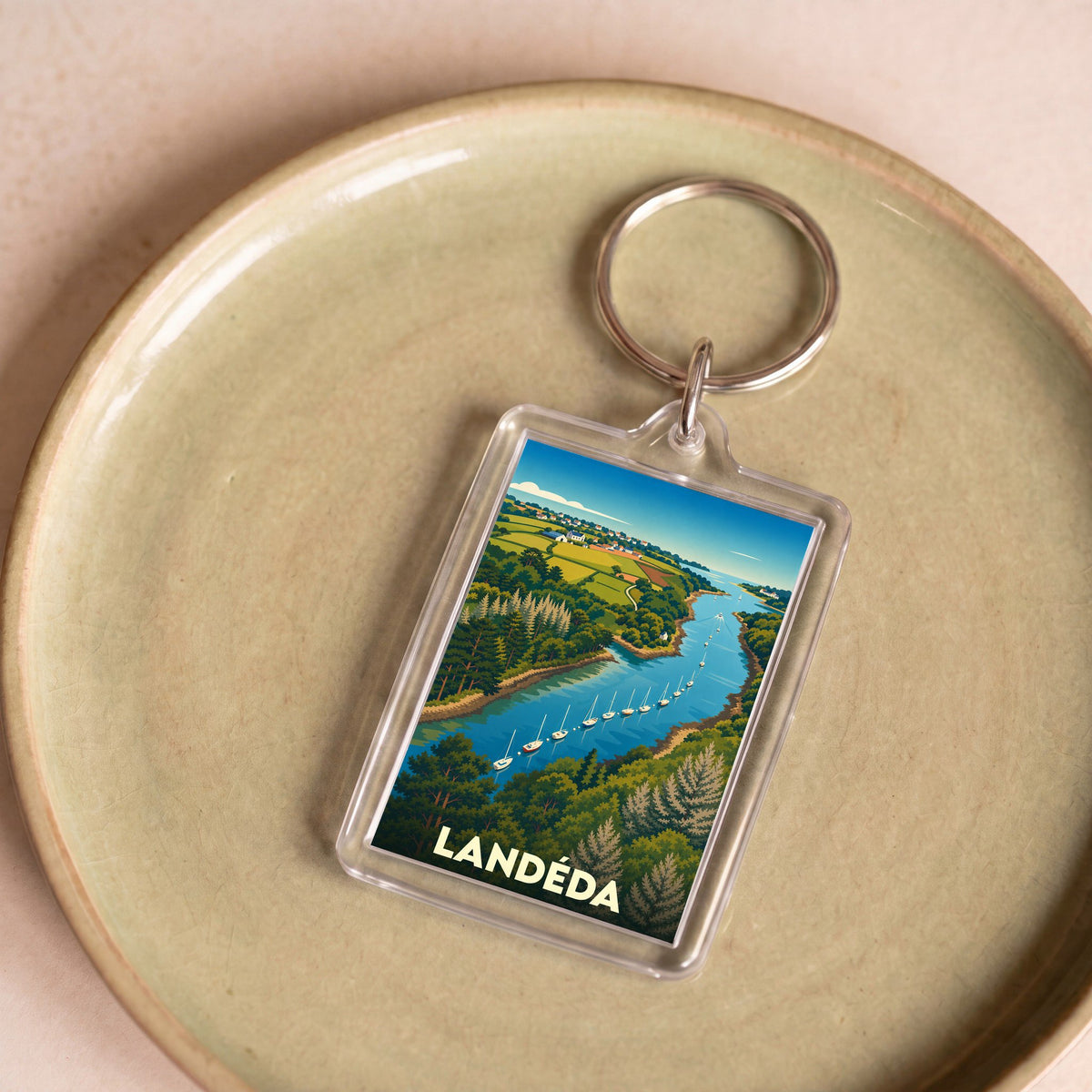Porte-clés souvenir de la ville de Landéda avec une illustration stylisée d'un bras de mer bordé de collines verdoyantes.