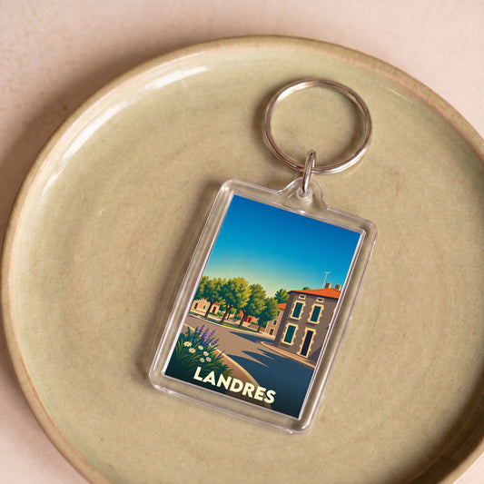 Porte-clés souvenir de la ville de Landres avec une illustration stylisée d'une rue ensoleillée.