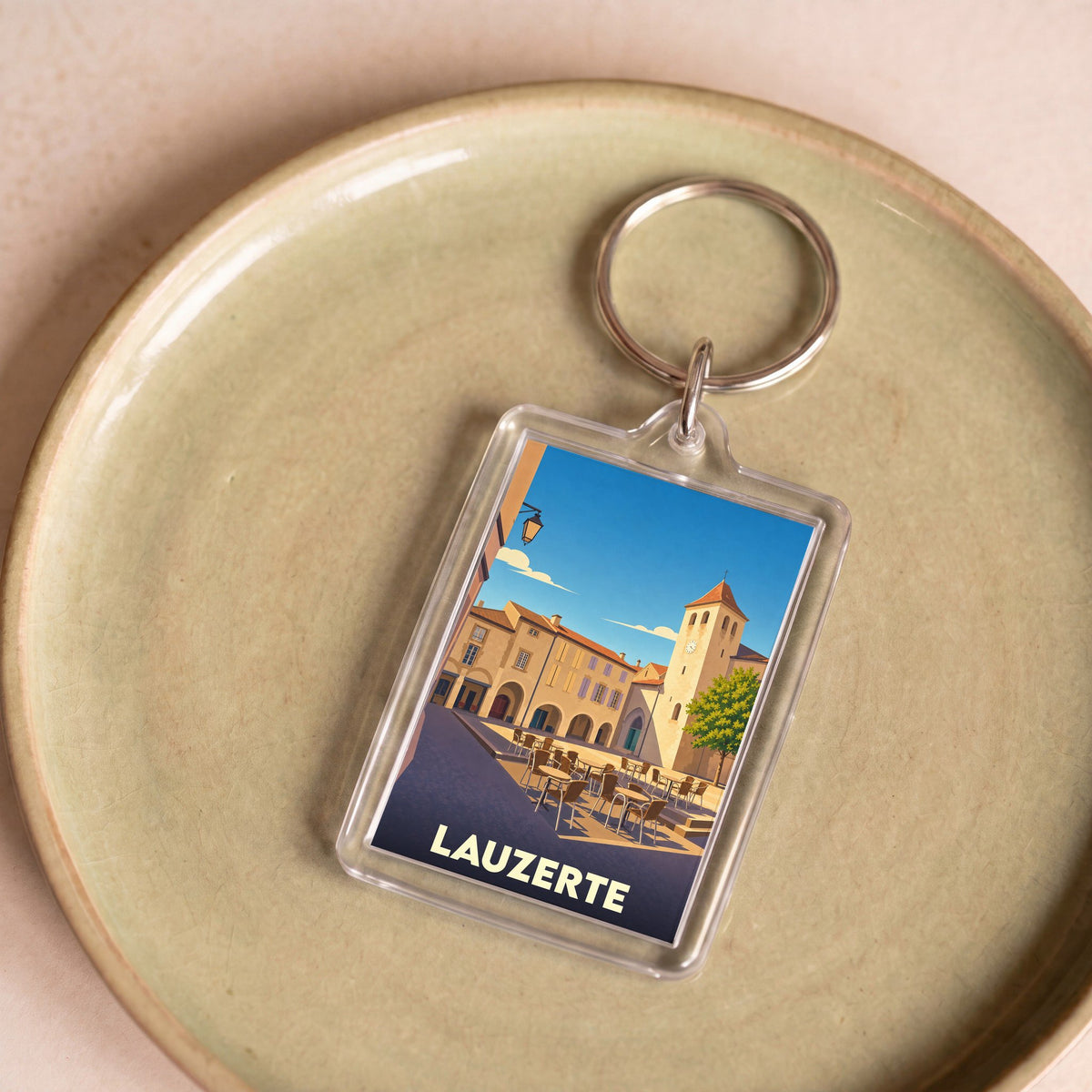 Porte-clés souvenir de la ville de Lauzerte avec une illustration stylisée de sa place centrale.