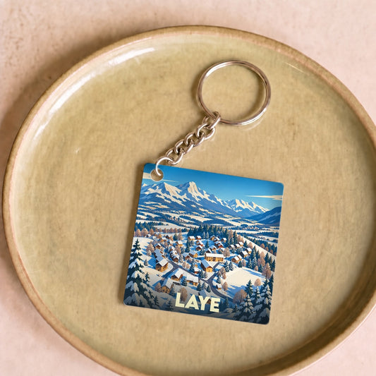 Porte-clés souvenir de la ville de Laye illustrant un paysage de montagne enneigé avec un village.