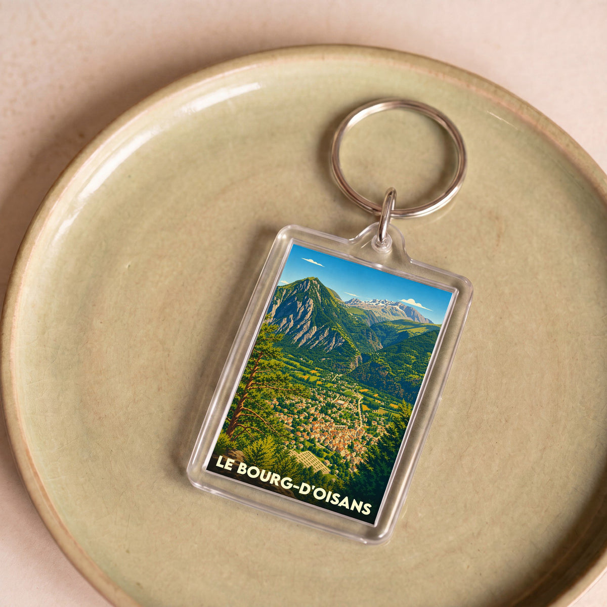 Porte-clés souvenir de Le Bourg-d'Oisans avec une illustration stylisée de la ville et des montagnes.