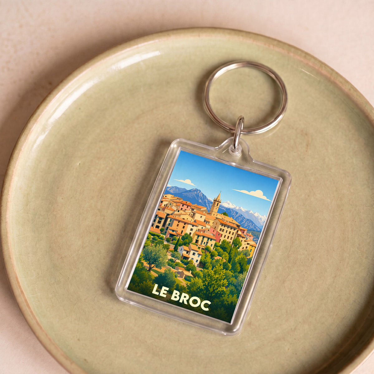 Porte-clés souvenir de la ville de Le Broc avec une illustration stylisée du village et des montagnes.